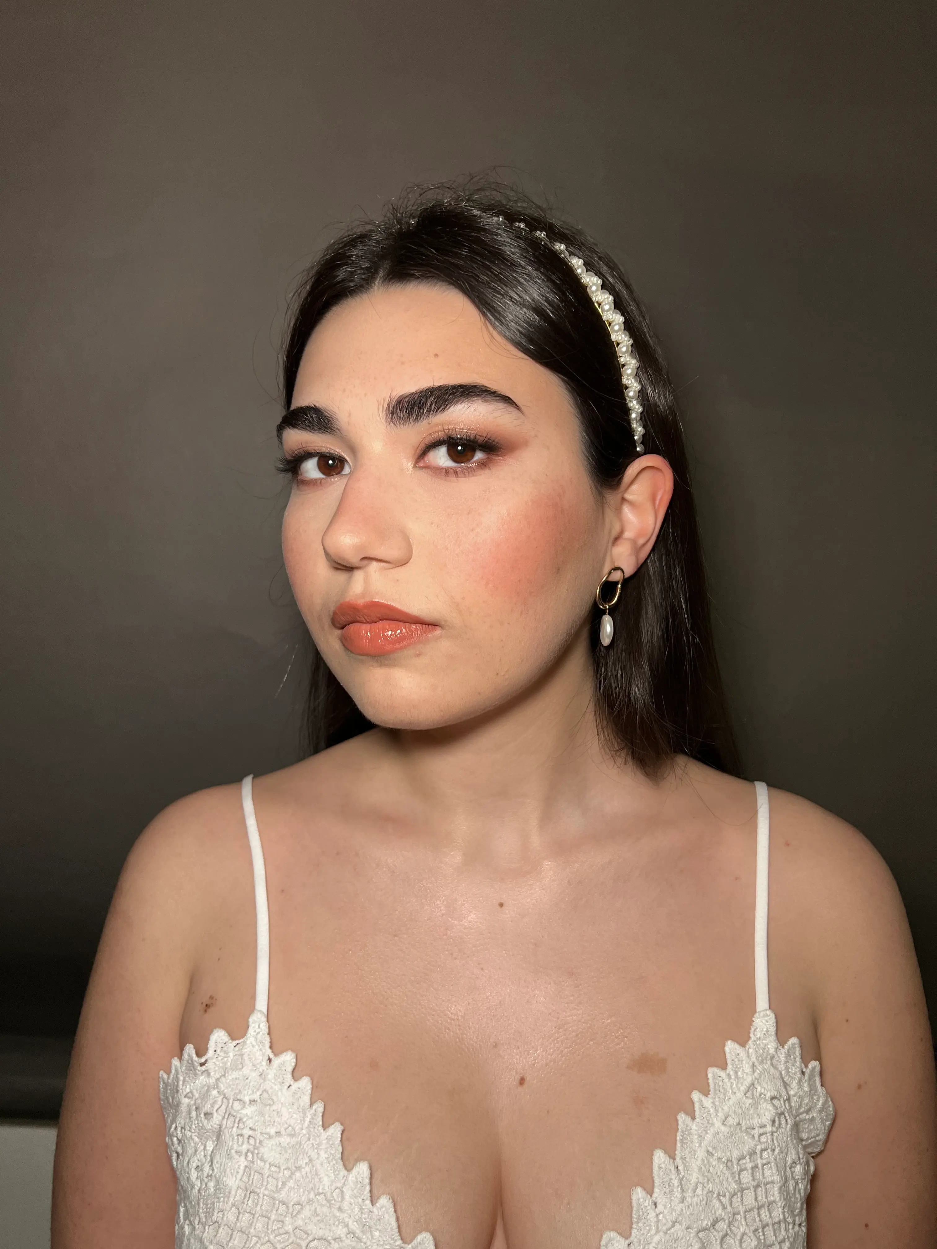Bridal look with a soft, radiant base, peach-toned blush, and warm eyeshadows that enhance the gaze, completed with glossy peach lips for a fresh and elegant finish.